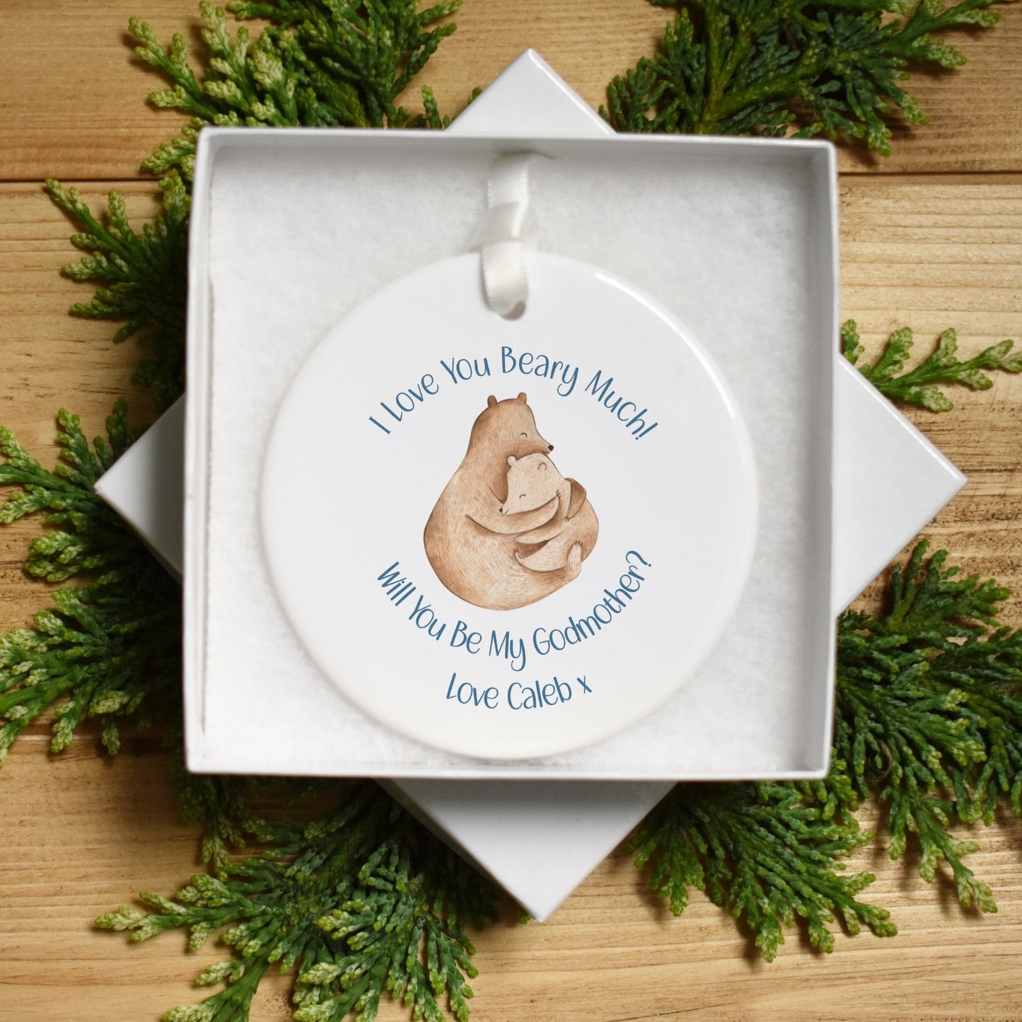 Image shows our white ceramic keepsake bauble with 2 bears in a watercolour painted cute style, hugging each other. Text printed onto the ceramic reads "I love you beary much! will you be my godmother?" With the personalised name underneath. The ceramic is approximately 7x7cms and 3mm in depth. It is a flat bauble, .