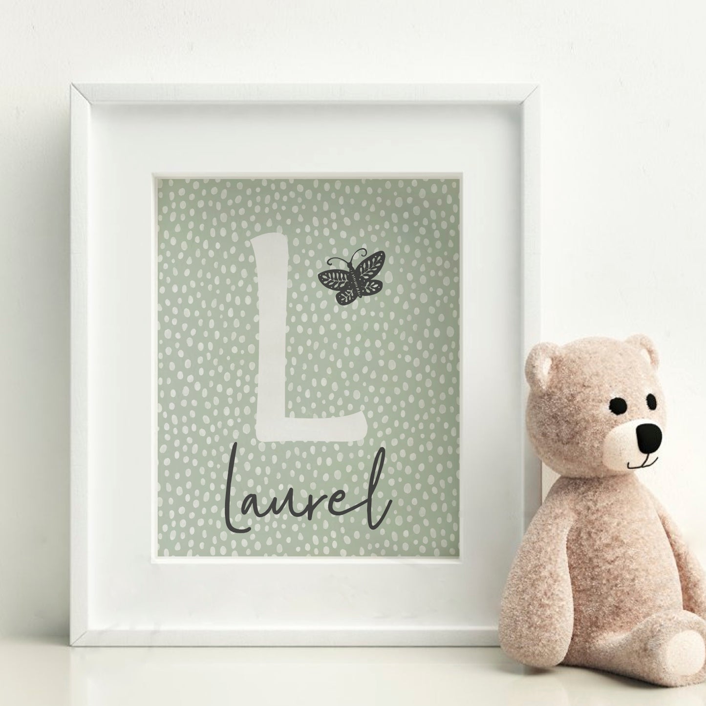 Image shows our Boho Sage Green Spotty Personalised wall print. The first letter of the child's name is centred in the middle, and is an off white colour. Underneath is the child's name in a handwritten script font. There is a simple, handrawn butterfly by the initial. 