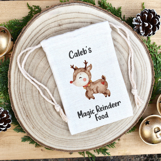 Image shows a personalised reindeer food drawstring pouch. The image is a cute reindeer with a red nose, in a watercolour style artwork. Above the Reindeer is the child's name which can be customised to one of your choosing, then underneath the reindeer are the words magic reindeer food. The bag comes filled with wildlife friendly wild bird seed.