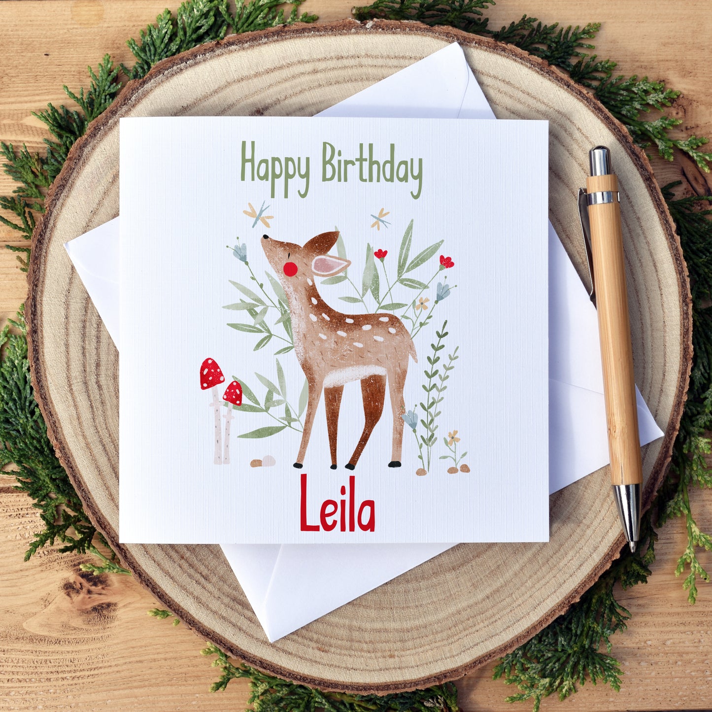 Personalised Woodland Deer Birthday Card. Beautifully illustrated deer or fawn, surrounded by green foliage, flowers and toadstools. The card has a white background. Our cards are approximately 6x6 inch and square in shape. We use high quality, textured card for printing to compliment the artwork style.  Our cards come with a white envelope and are packaged with biodegradable, eco friendly cellophane for protection from water damage during shipping. 