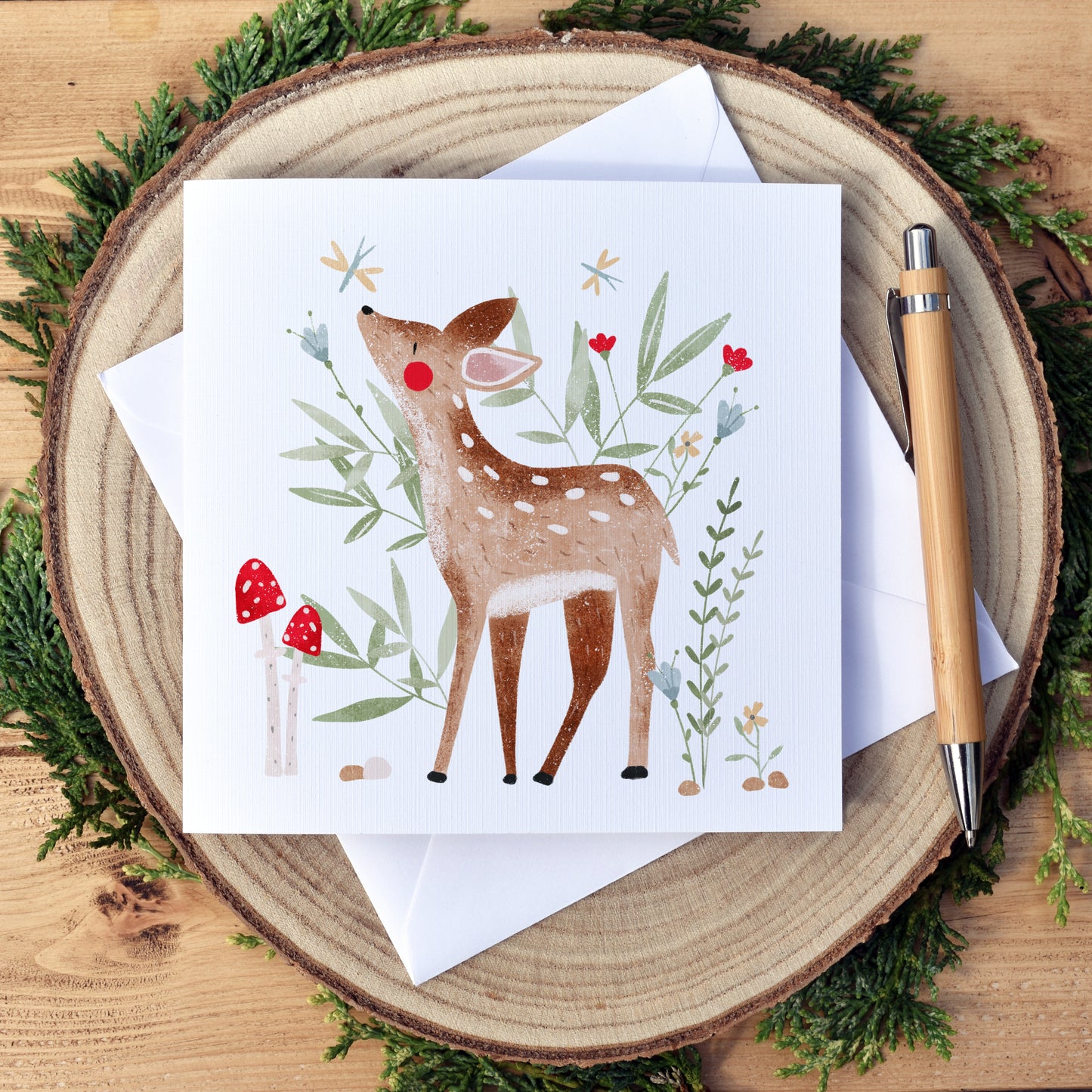 Plain Woodland Deer Birthday Card. Beautifully illustrated deer or fawn, surrounded by green foliage, flowers and toadstools. The card has a white background. Our cards are approximately 6x6 inch and square in shape. We use high quality, textured card for printing to compliment the artwork style. Our cards come with a white envelope and are packaged with biodegradable, eco friendly cellophane for protection from water damage during shipping.